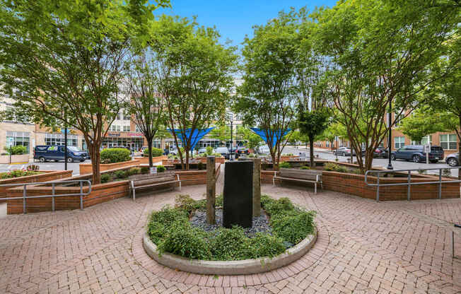 A park with a fountain surrounded by benches and trees.