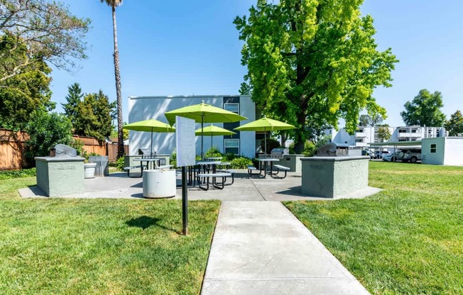 A sunny day at a park with picnic tables and green umbrellas.
