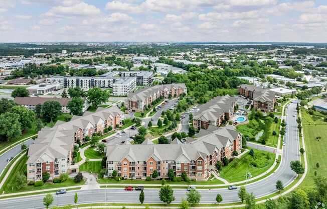 A large apartment complex with a swimming pool is surrounded by a green lawn and trees.