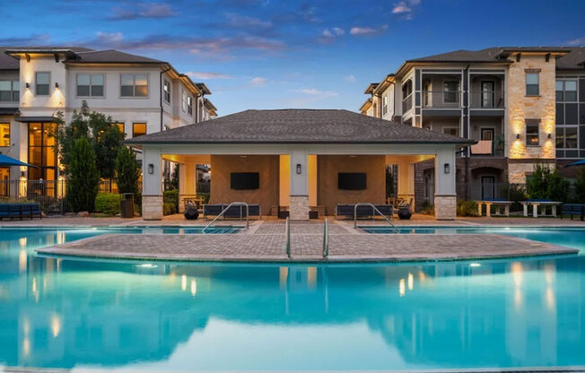 A swimming pool in front of a building with a patio and a barbecue grill.