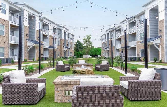 an outdoor lounge area with chairs and a fire pit in front of an apartment complex