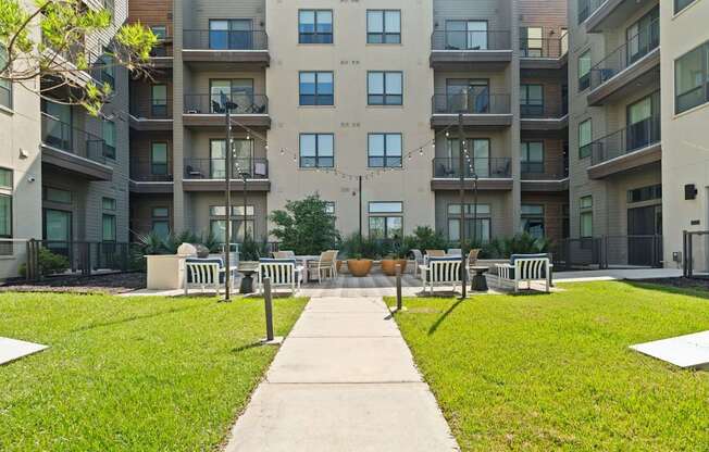 A concrete walkway leads to a grassy area with benches in front of apartment buildings.