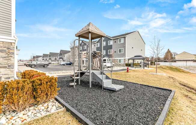 A playground with a slide and a swing set in the foreground and apartment buildings in the background.