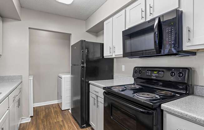 A black refrigerator and stove in a kitchen with white cabinets.