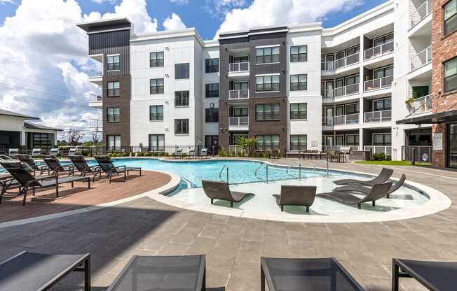 a swimming pool with lounge chairs in front of an apartment building