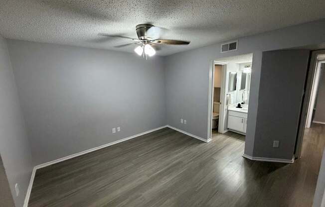 A room with a ceiling fan and light, wooden floors, and a white door.