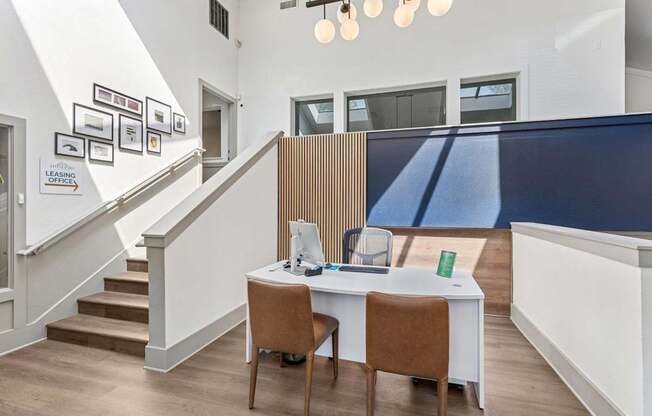 A room with a desk and chairs and a staircase.