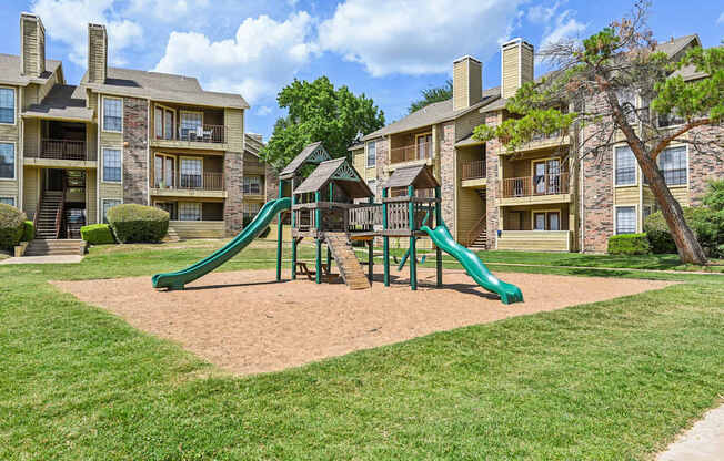 A playground with a green slide in front of apartment buildings.