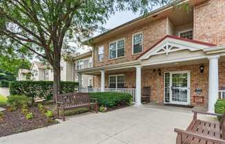 A brick house with a porch and a tree in front.