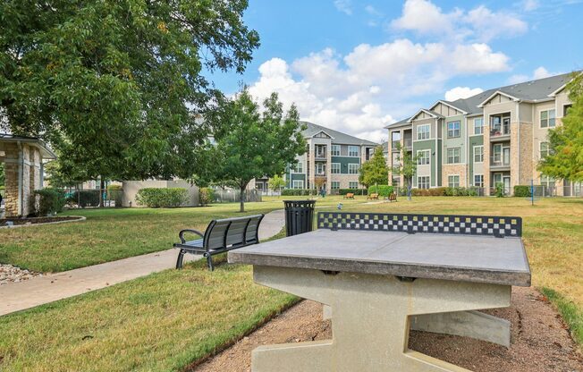 A concrete bench with a black and white checkered back sits in a grassy area.