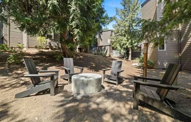 Firepit with four chairs and a table in the middle of a dirt area with trees  at Larkspur West Linn, Oregon