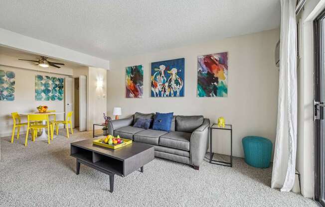 A living room with a grey couch, a yellow dining table, and a painting on the wall.