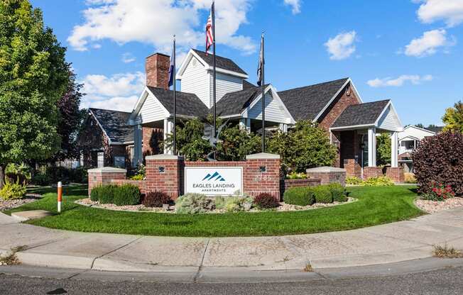 Entrance to community with welcoming flags, mainucured greenery, and building signage at Eagles Landing, Ammon