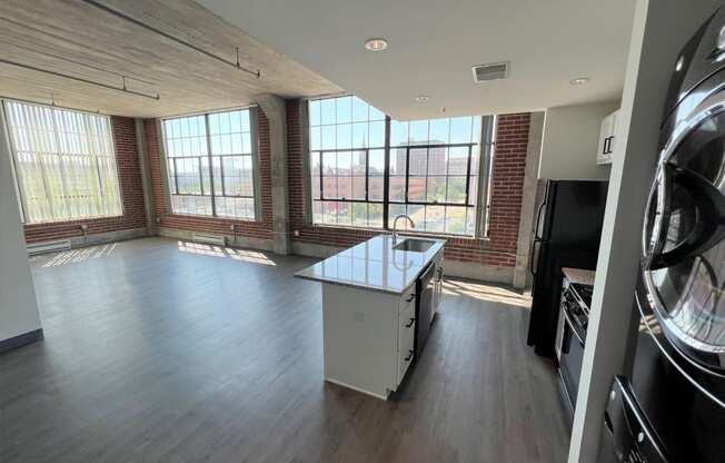 an empty living room with a kitchen and large windows