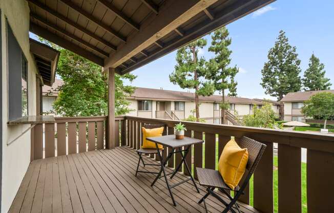 two chairs with yellow pillows sit on a wooden deck with trees in the background