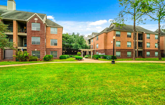 A large grassy area in front of two red brick apartment buildings.