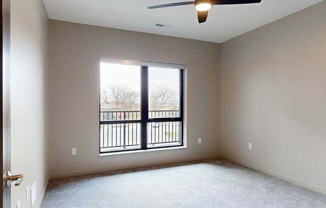 a bedroom with a ceiling fan and a large window overlooking a balcony