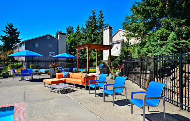 A poolside area with blue chairs and a wooden pergola.