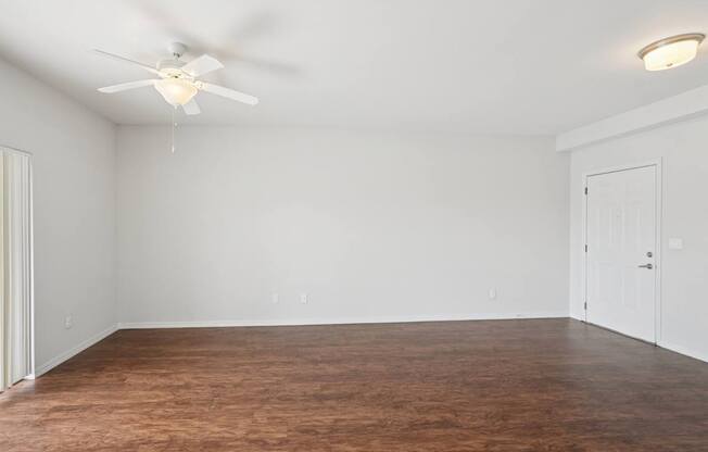 A room with a ceiling fan and brown flooring.