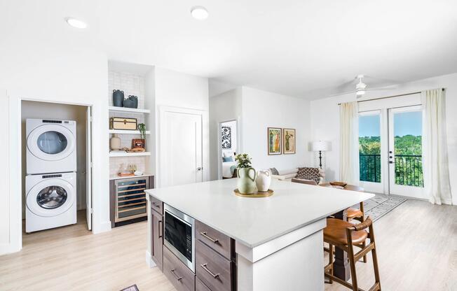 Open kitchen with a large island, built-in wine storage, and seamless flow to a bright living area with balcony views and in-home front loading washer and dryer.