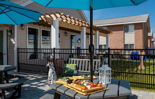 A picnic setup on a patio with a blue umbrella and a tray of food.