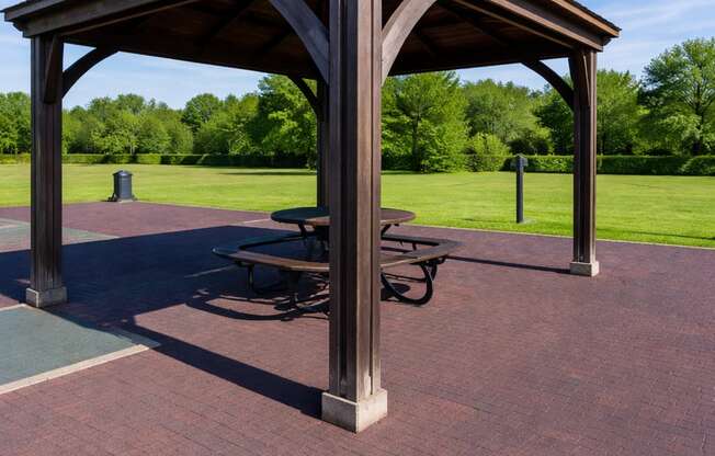 A wooden pavilion with a picnic table sits in a park.