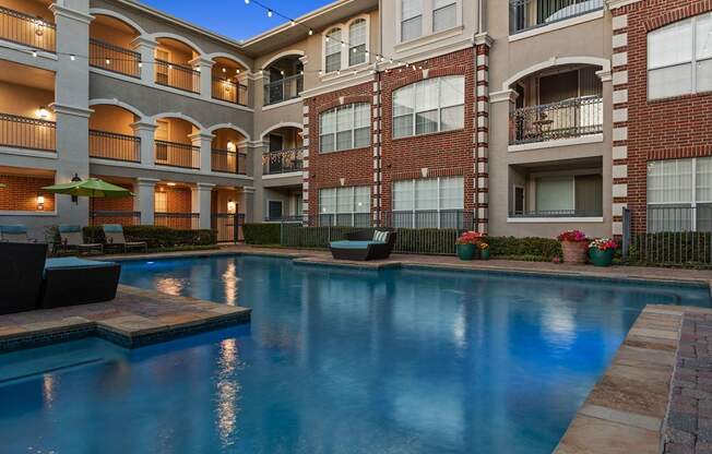 A large swimming pool in front of a brick building with balconies.