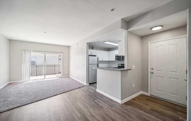 an empty living room and kitchen with a door to a balcony