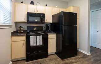 A black refrigerator stands next to a black stove in a kitchen.