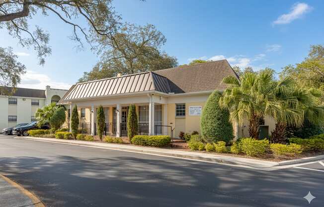 A building with a white facade and a black roof is surrounded by greenery.