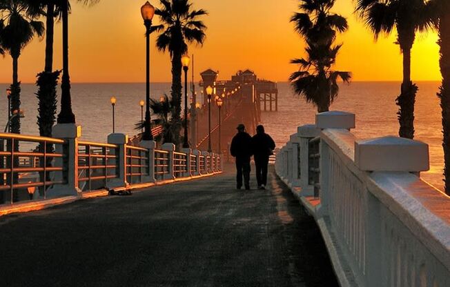 two people walking down a pier at sunset
