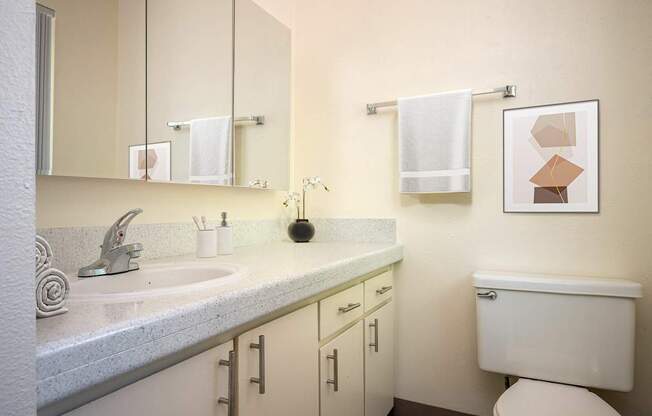 A bathroom with a toilet, sink, and cabinets.