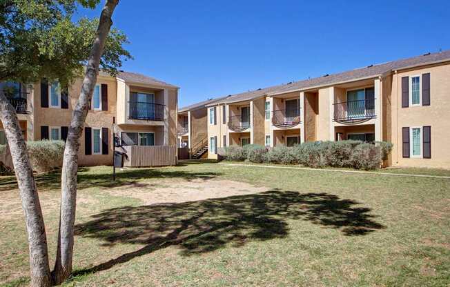 A peaceful apartment courtyard here at Avalon Springs with two-story buildings, private balconies and patios, open green lawn space, and mature trees that create a relaxed, neighborhood-style setting.