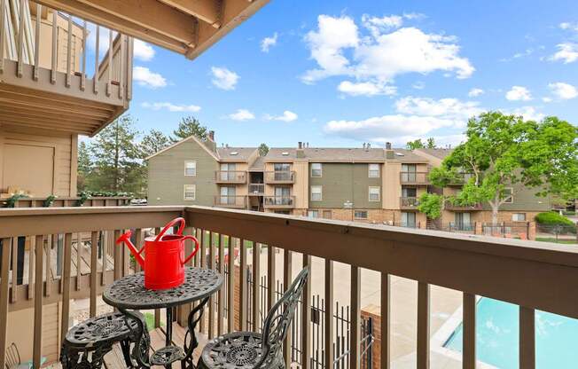 A red watering can sits on a table on a balcony.