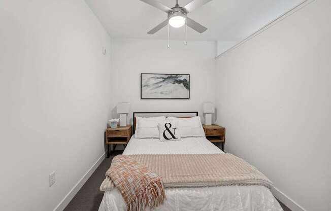A bedroom with a bed, a ceiling fan, and a painting on the wall.