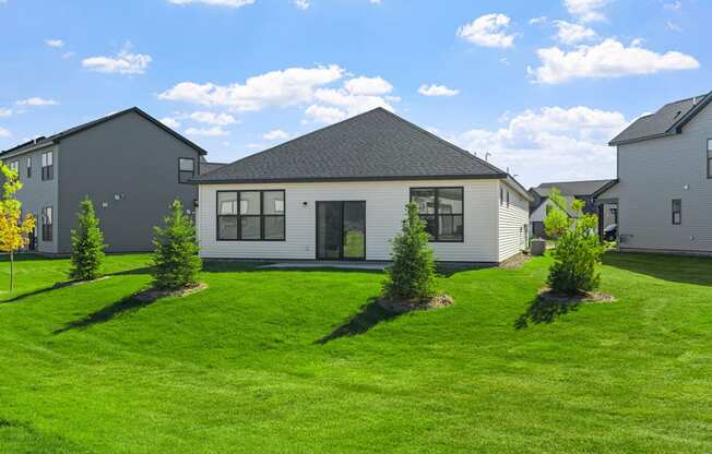 the front of a house with a green lawn and some small trees