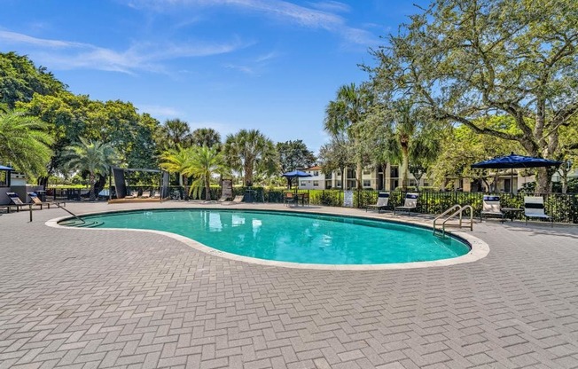 A swimming pool surrounded by a brick patio and trees.