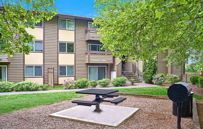 Exterior view of patio area and BBQ, manicured grounds and building, and blue skies in the background at Heritage Grove, Renton, WA.