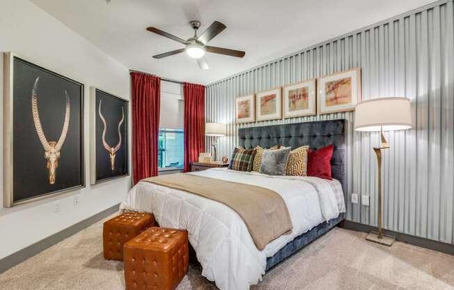 A bedroom with a bed, a ceiling fan, and a painting of an animal skull on the wall.