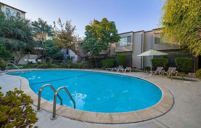 A swimming pool surrounded by trees and chairs.