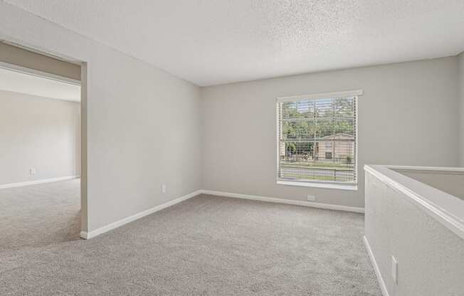 A room with a carpeted floor and a window showing a view of a house.