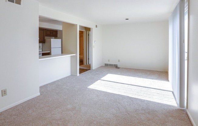 an empty living room with a kitchen in the background