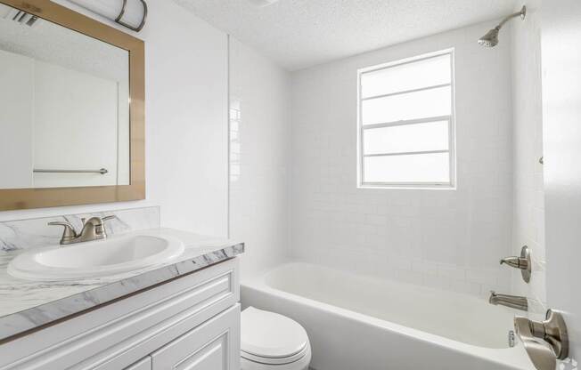 A white bathroom with a marble countertop and a large mirror.
