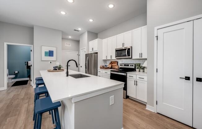 a kitchen with white cabinetry and a large white island with a sink and three stools