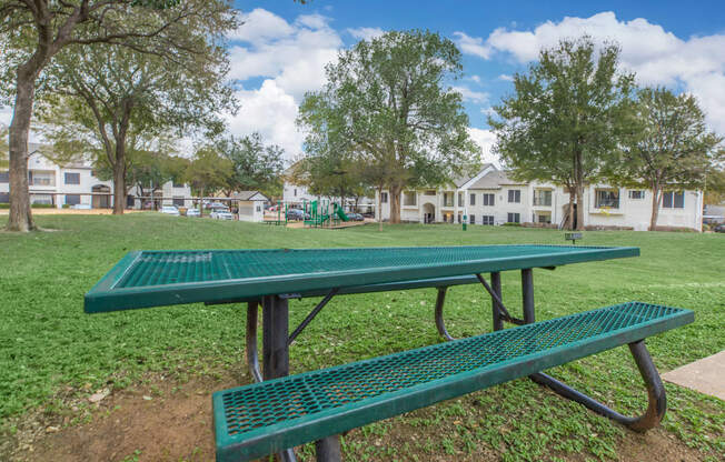 a green ping pong table in a park with a playground in the background