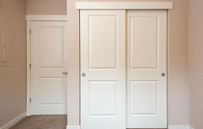 a closet with two white doors and a door to a hallway