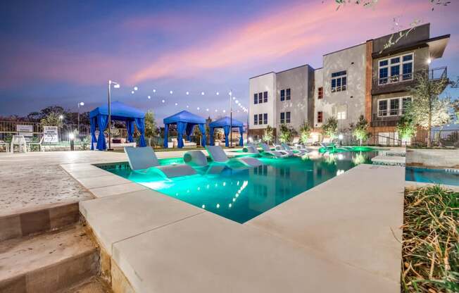 A swimming pool area with a building in the background at dusk.