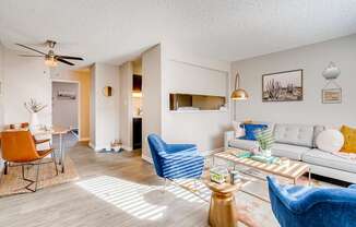 A living room with a white couch, blue armchair, and a coffee table at Mountain Vista Apartments, Colorado