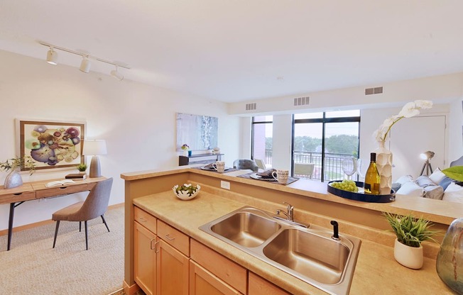 A kitchen with a sink with a desk and chair in the adjacent space.