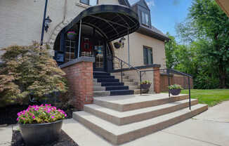 A house with a black awning and a brick pillar with steps leading up to the door.